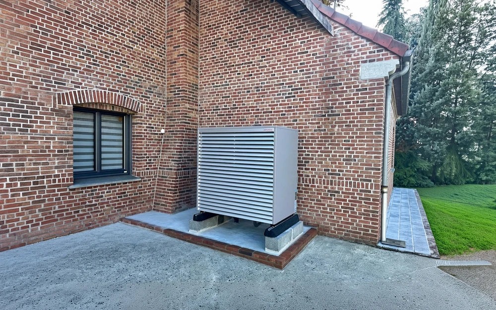 Unité extérieure de pompe à chaleur air/air installée contre un mur en briques rouges d'une maison individuelle