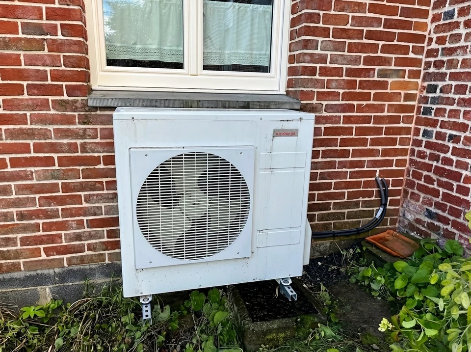 Extérieur résidentiel avec pompe à chaleur air-eau installée sur terrasse pavée contre mur de briques