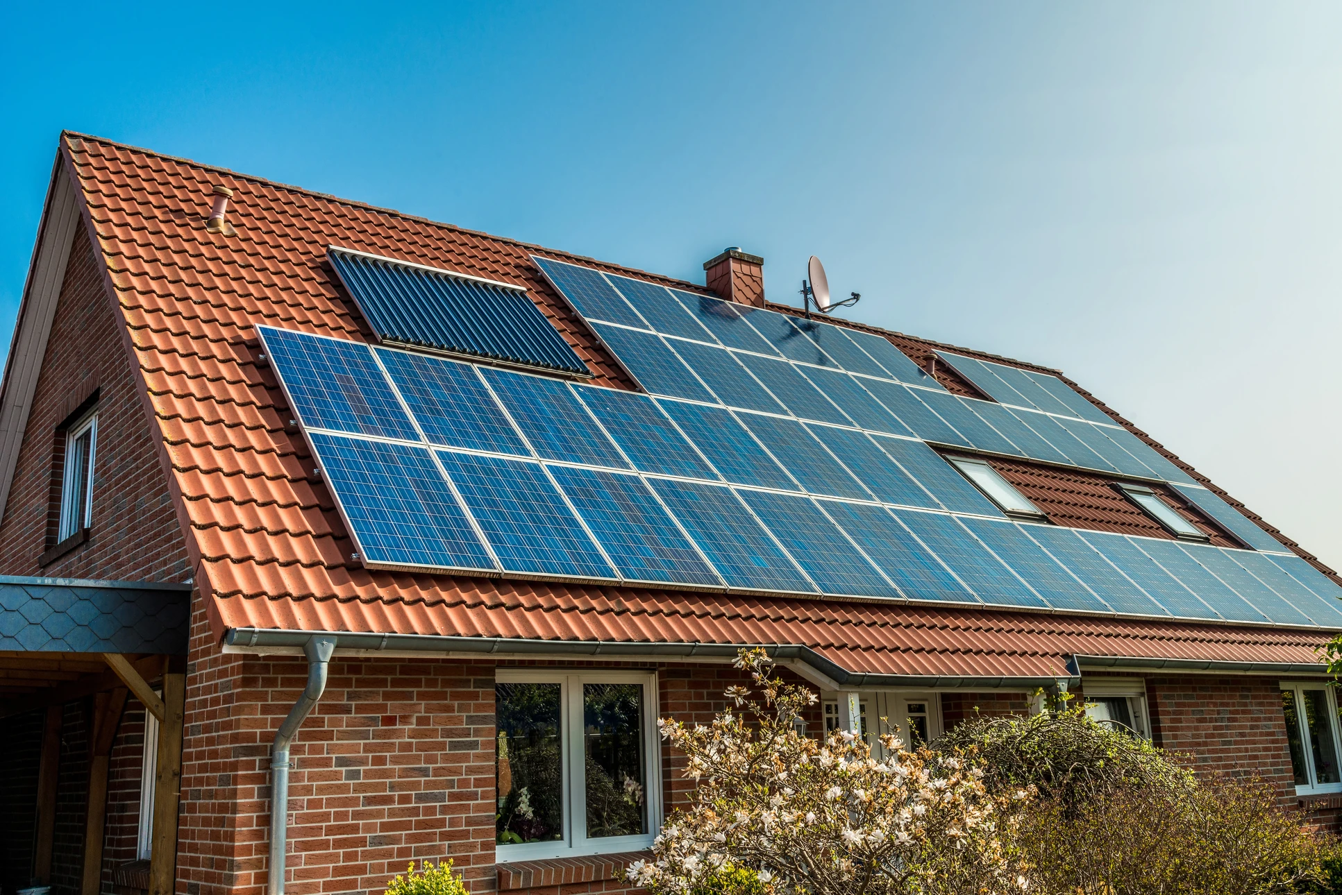 Maison résidentielle en brique rouge avec toiture en tuiles équipée de panneaux solaires photovoltaïques et capteurs solaires thermiques