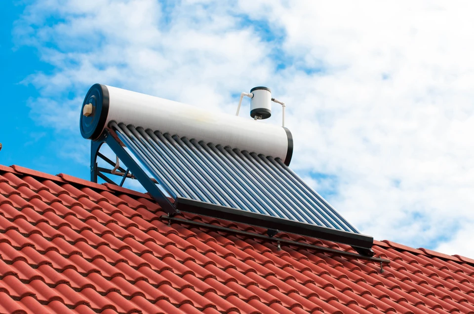 Toiture résidentielle équipée de quatre chauffe-eau solaires thermiques installés sur tuiles rouges, ciel bleu dégagé en arrière-plan avec maisons voisines visibles